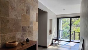A modern interior with a stone wall, a wooden bench, and a view of greenery outside.