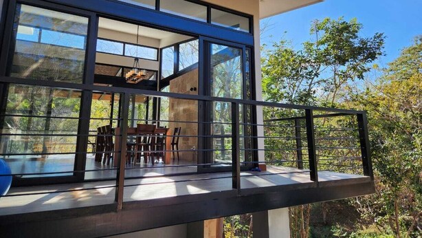 A modern house with large glass windows, a balcony, and a dining area with outdoor furniture.