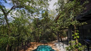 An outdoor swimming pool surrounded by trees, with a wooden deck and a bench.