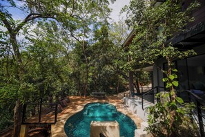 An outdoor swimming pool surrounded by trees, with a wooden deck and a bench.