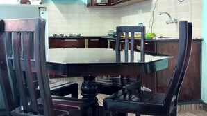 Un comedor con una mesa y sillas de madera, una zona de cocina con armarios y un techo con viga de madera.