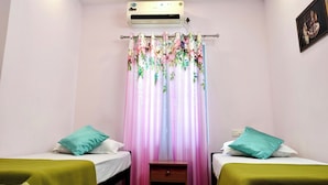Un dormitorio con dos camas individuales, una mesita de noche pequeña, un aire acondicionado instalado en la pared y una cortina con motivos florales.