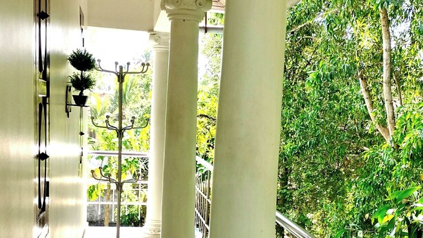Un pasillo con columnas blancas, barandilla de metal y vistas al exterior con follaje.