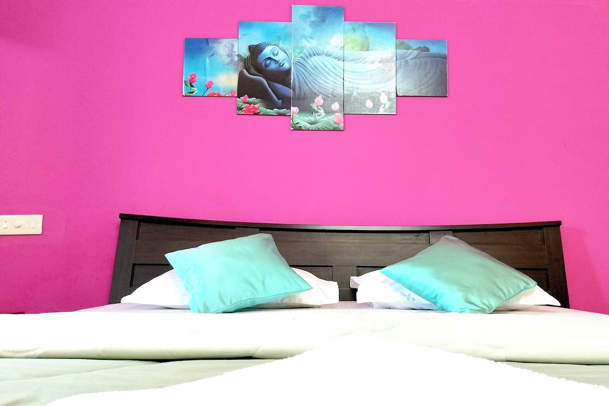Ein Bett mit zwei Kissen, einem Holz-Kopfteil und einer rosa Wand mit einem gerahmten Bild darüber.