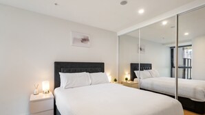 A modern bedroom with a large bed, a nightstand with a lamp, and a mirror reflecting the room. - City Views & Inner-north Cool at Your Door (Melbourne)