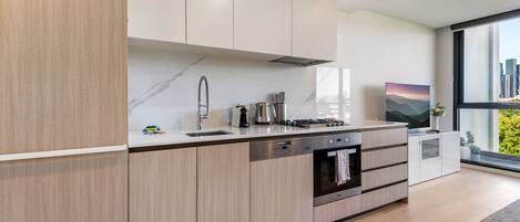 A modern kitchen with light wood cabinets, stainless steel appliances, and a large window offering a city view.