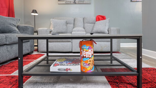 Olohuoneessa on harmaa sohva, punainen koristetyyny, lasinen sohvapöytä, jonka päällä on Jenga-peli ja Connect 4 -peli.