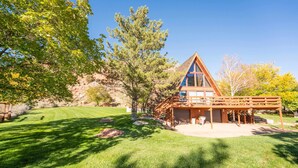 A log cabin with a large glass front, a deck, and a well-maintained lawn. - Family Cabin w/Hot Tub | Red Rock Views | Pets (Kanab)