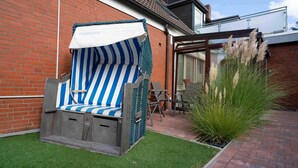 A striped outdoor chair with a canopy, a brick wall, and a potted plant. - Gemuetliche Ferienwohnung mit Wintergarten, Bensersiel (Esens)