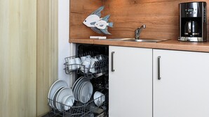 A compact kitchen with a dishwasher, a coffee maker, and a decorative fish on the wall. - Gemuetliche Ferienwohnung mit Wintergarten, Bensersiel (Esens)