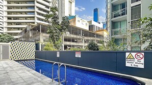 A swimming pool with a no diving warning sign, surrounded by modern buildings and a tiled walkway.