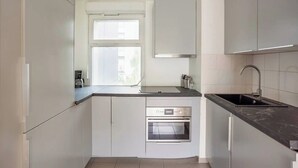 Una cocina moderna con armarios blancos, horno empotrado, encimera negra y una ventana que proporciona luz natural.