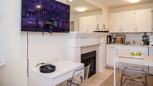 Una cocina moderna con gabinetes blancos, una chimenea, una mesa de comedor con sillas y un televisor de pantalla plana montado en la pared.