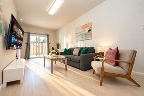 A modern living room with a sofa, a coffee table, and a TV mounted on the wall. - Central 3BR Home - Steps from Mountain View DT, Castro St (Mountain View)