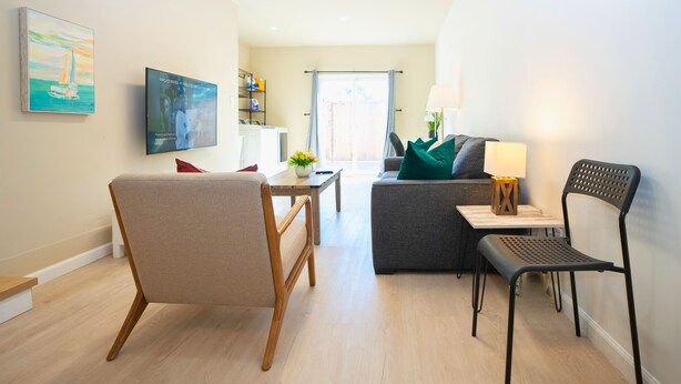 A modern living room with a sofa, a chair, a TV, and a dining area with a table and chairs. - Central 3BR Home - Steps from Mountain View DT, Castro St (Mountain View)