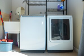 A laundry area with two white washing machines, a metal shelf with cleaning supplies, a mop, and a broom. - Central 3BR Home - Steps from Mountain View DT, Castro St (Mountain View)