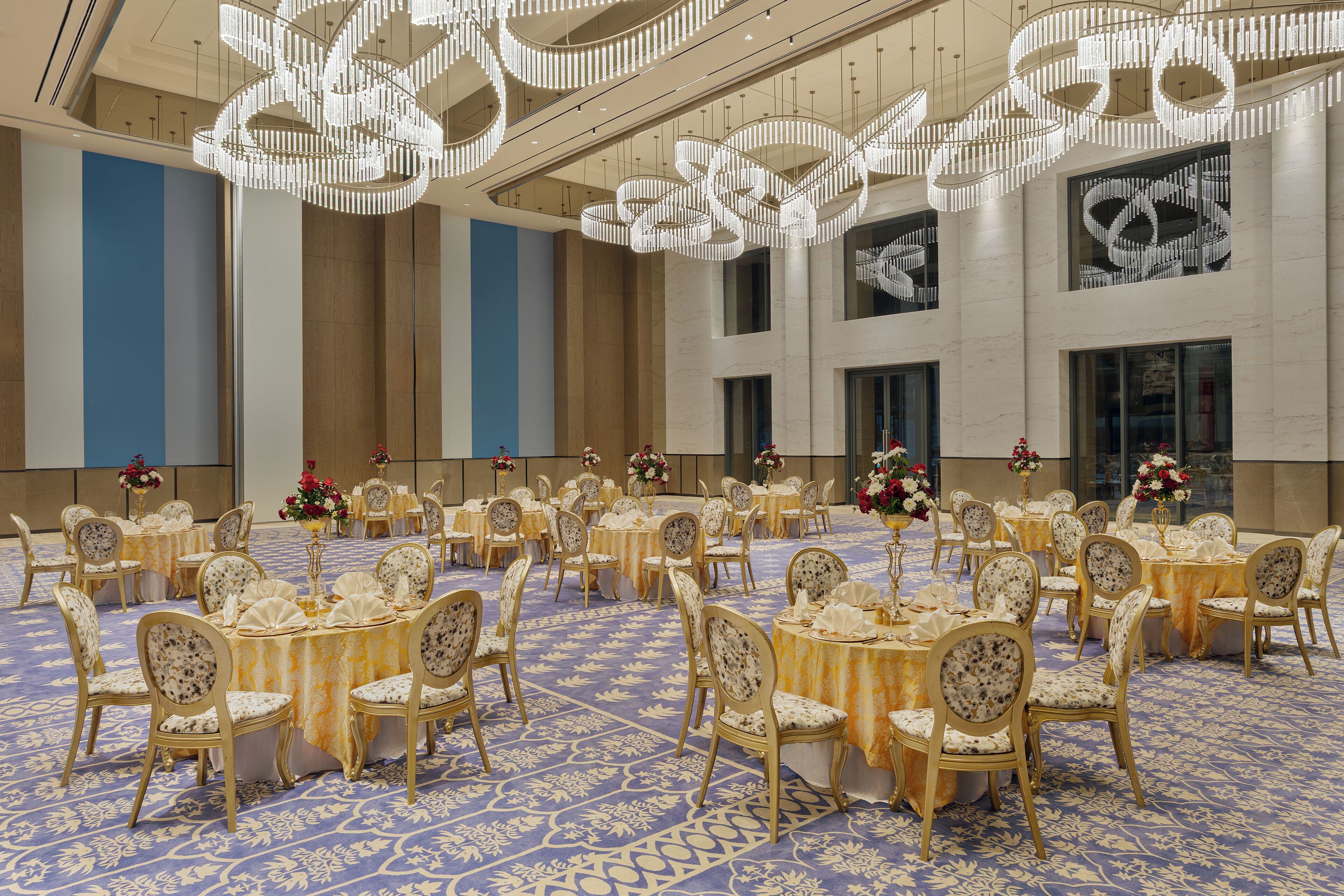 A banquet hall with round tables, chairs, and a blue patterned carpet.