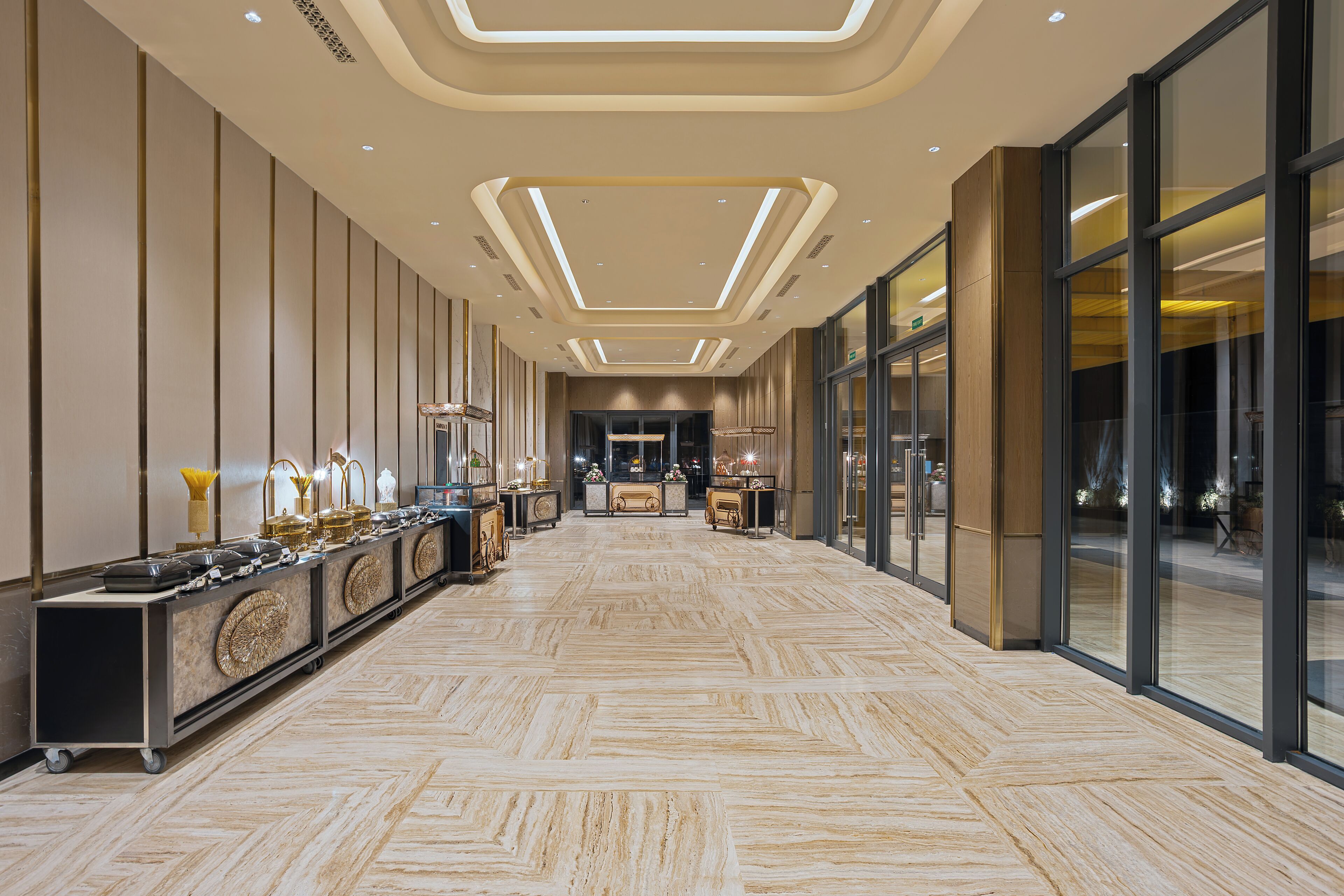 Un couloir d’hôtel avec un long comptoir de réception, un sol à motifs en chevrons et un design moderne au plafond.