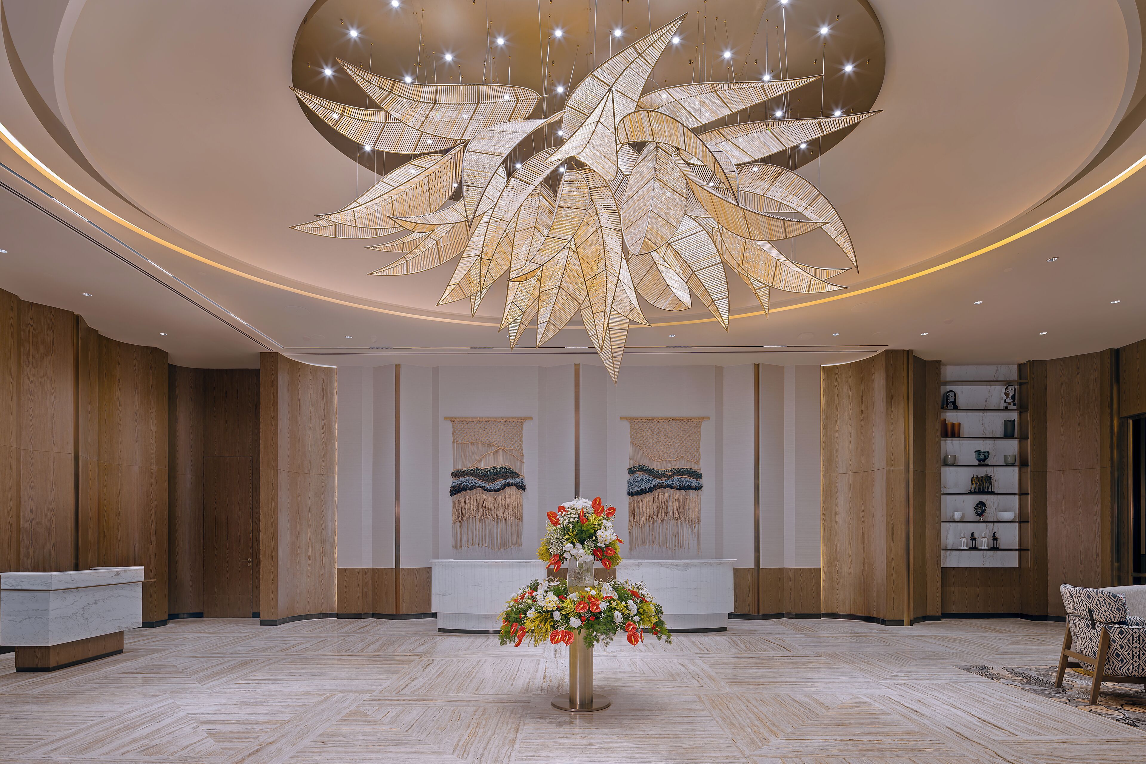 A lobby with a reception desk, a large decorative ceiling piece, and a floral arrangement.