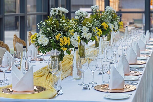 A long table set for a formal event with multiple place settings, each with a folded napkin, a glass, and a gold-colored plate.