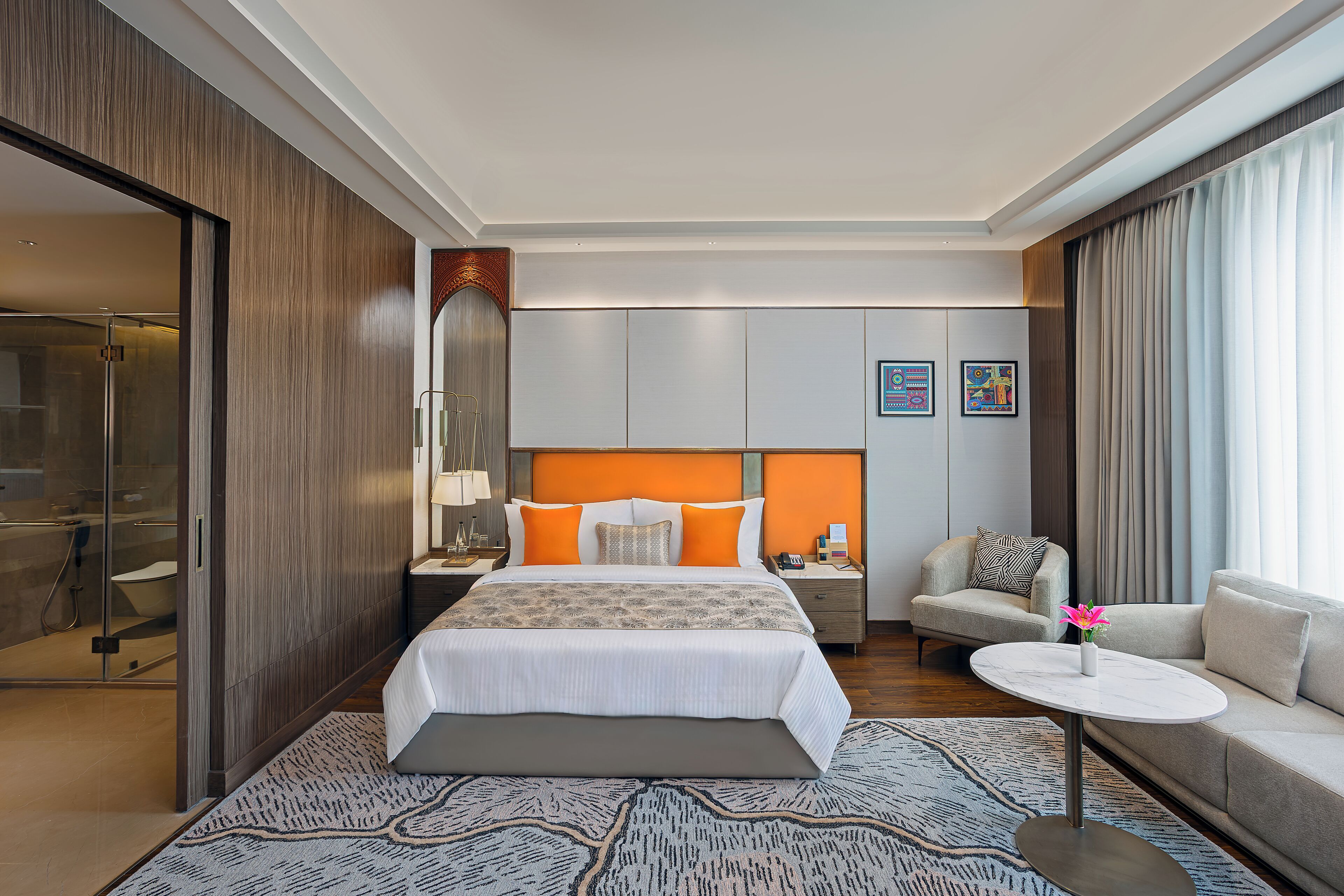A hotel room with a bed, a sofa, a small table, a nightstand, a bathroom, and a large window.