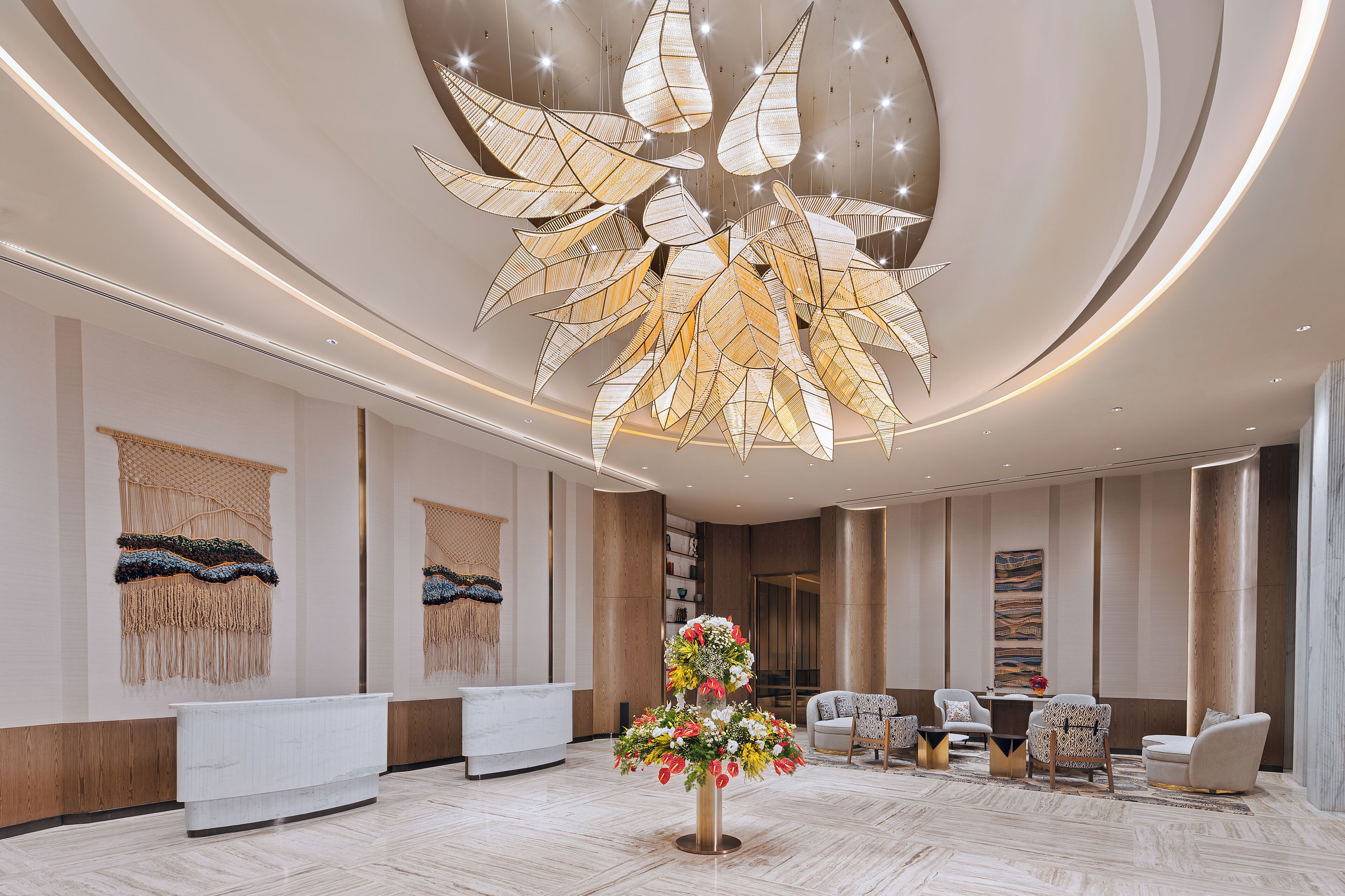 A modern lobby with a central floral arrangement, a reception desk, seating area, and a unique ceiling light fixture.