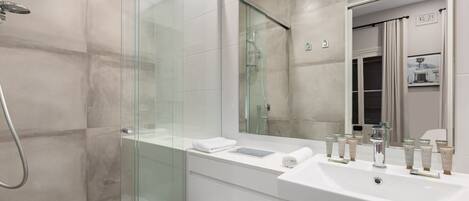 Une salle de bain moderne avec une douche à parois de verre, un grand miroir et un lavabo blanc agrémenté de nombreux accessoires de toilette.