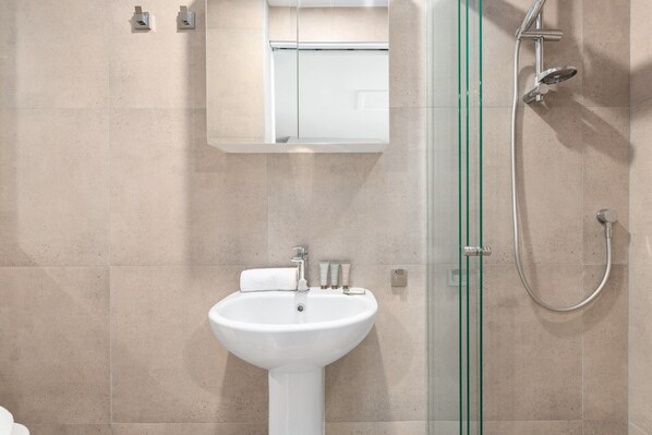 A modern bathroom with a white sink, glass shower enclosure, and a mirror above the sink. - Spacious Inner-city House With Balcony Views (Sydney)