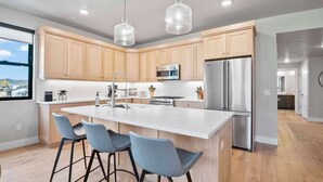 Una cucina moderna con mobili in legno, elettrodomestici in acciaio inossidabile, un'isola centrale con sgabelli da bar e illuminazione a sospensione.