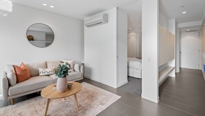 A modern living room with a sofa, coffee table, and a round mirror on the wall. - Chic City Escape With Pool, Gym & Parking (Melbourne)