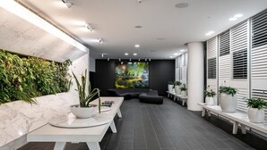 A modern lobby with a marble wall, a green vertical garden, a large abstract painting, and a seating area with benches and potted plants. - Chic City Escape With Pool, Gym & Parking (Melbourne)