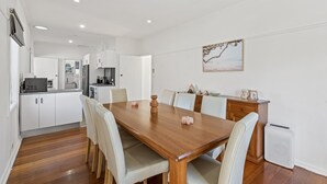 A modern kitchen with white cabinets, a wooden dining table, and a white refrigerator. - Spacious 3-bed With Outdoor Dining Near Airport (Melbourne)