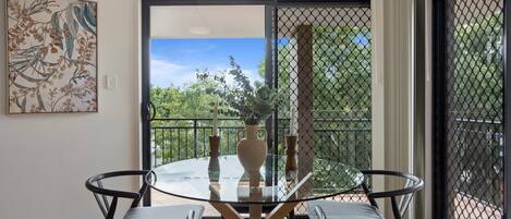 A room with a glass table and four chairs, a vase, and a painting on the wall.