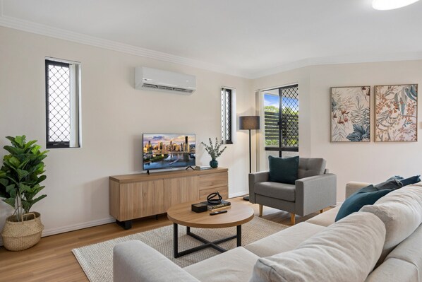 A modern living room with a sofa, a coffee table, a TV, and a cabinet. - Comfy 2-bedroom Family Apartment With Free Parking (Brisbane)