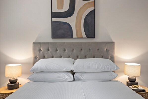 A neatly made bed with a tufted headboard, two bedside lamps, and a wall art piece above. - Comfy 2-bedroom Family Apartment With Free Parking (Brisbane)