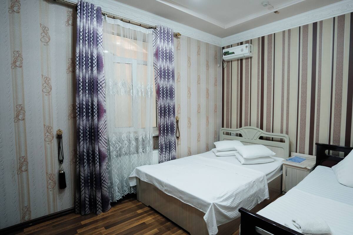 Une chambre d’hôtel avec deux lits, un plancher en bois, un papier peint à rayures et une fenêtre avec des rideaux.