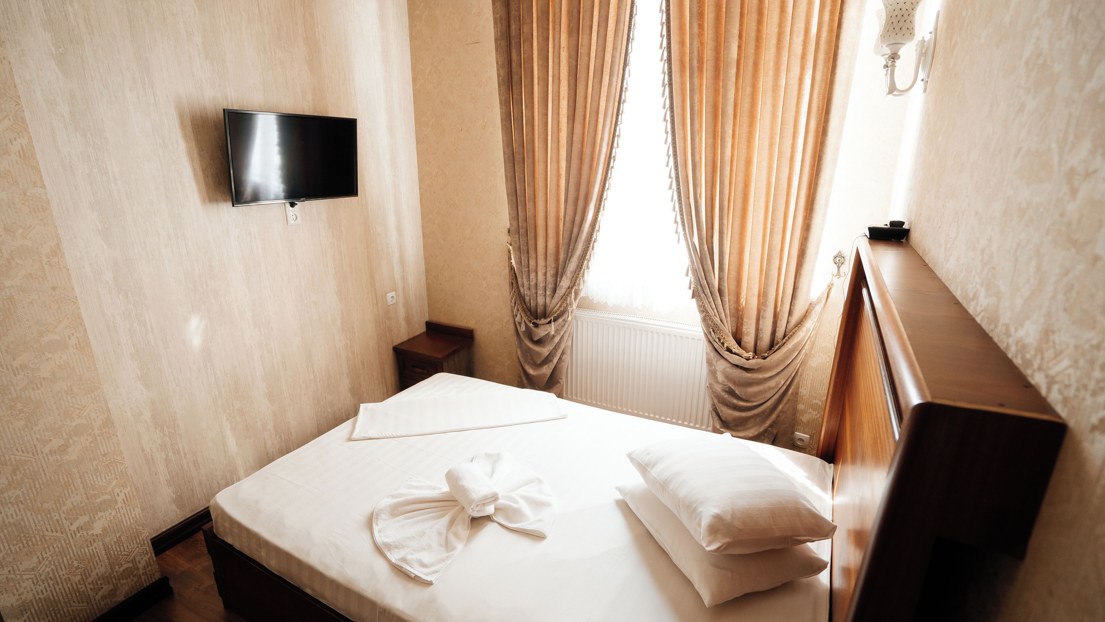 Quarto de hotel com cama, televisão de tela plana na parede e janela com cortinas.