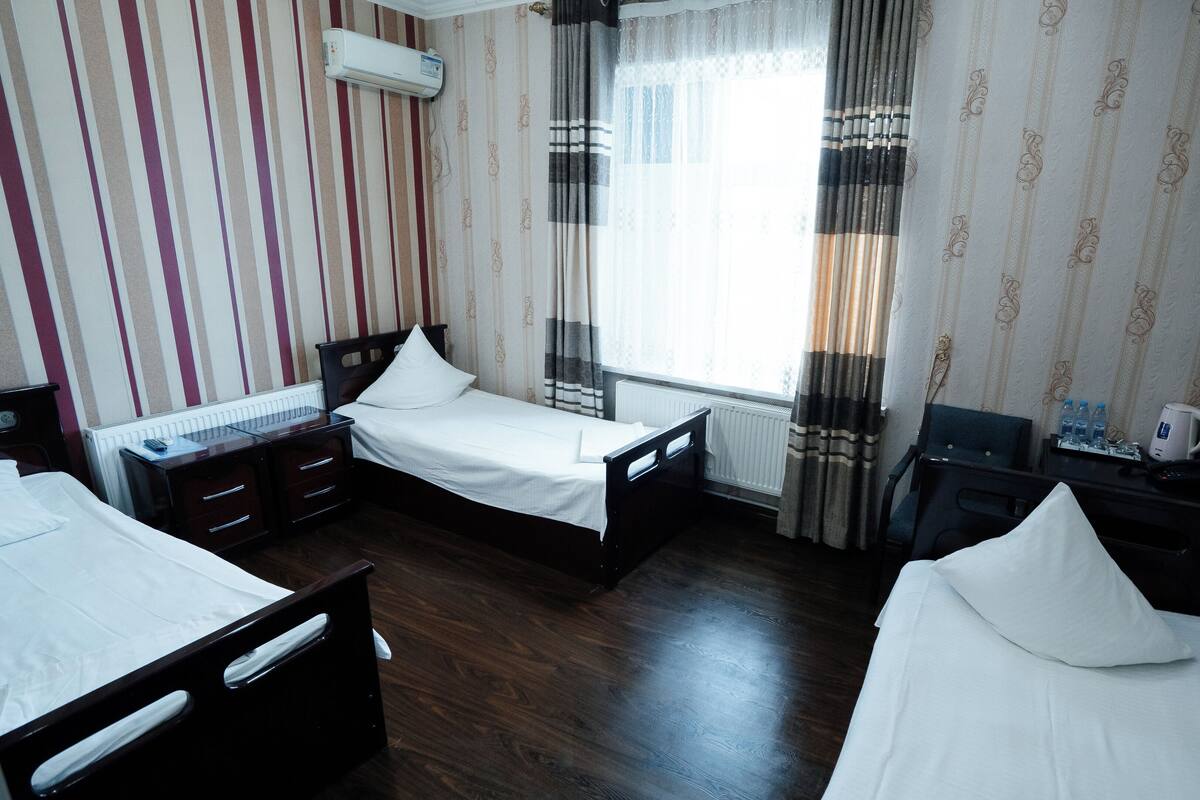 Une chambre d’hôtel avec deux lits simples, un bureau avec une chaise, une télévision et une fenêtre avec des rideaux.