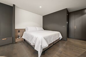A modern bedroom with a large bed, dark walls, and a wooden floor.