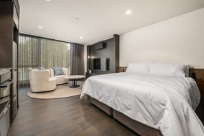 A modern hotel room with a large bed, a sofa, a small table, and a TV mounted on the wall.