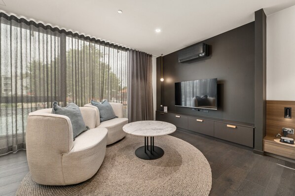 A modern living room with a sofa, a round coffee table, and a flat-screen TV mounted on the wall.