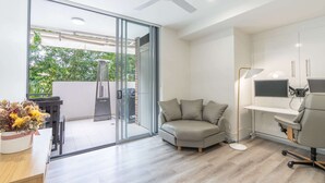 A modern office space with a sliding glass door leading to a balcony, a desk with a computer, and a comfortable seating area.