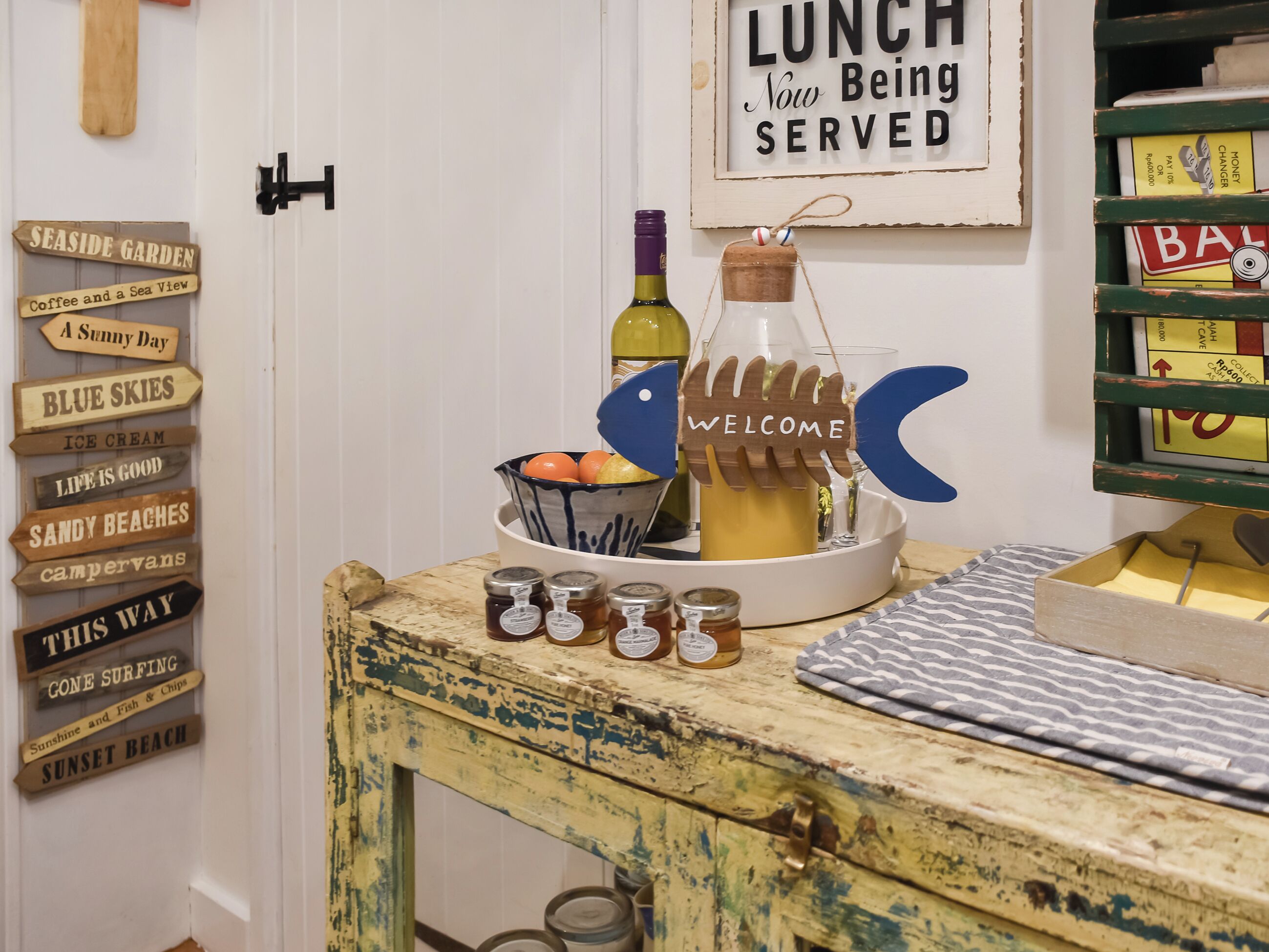 A rustic wooden table with a sign reading "LUNCH Now Being SERVED" and a welcome sign shaped like a fish.