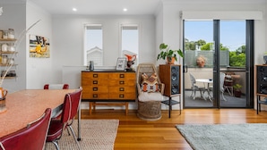A modern dining area with a wooden table and chairs, a built-in wooden cabinet, and a view through a glass door to an outdoor patio. - Charming Retro Townhouse in Vibrant Coburg (Melbourne)