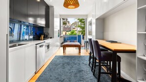 A modern kitchen with white cabinets, a wooden dining table, and a blue rug. - Elegant 1-bed With Study by Balmain Wharf (Sydney)
