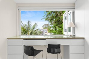 Una cocina moderna con un gran ventanal, dos sillas negras y una encimera blanca.