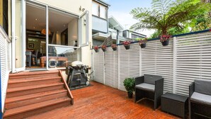 A wooden deck with outdoor furniture, a barbecue grill, and a white fence with potted plants. - Elegant 1-bed With Study by Balmain Wharf (Sydney)