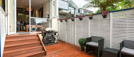 A wooden deck with outdoor furniture, a barbecue grill, and a white fence with potted plants.