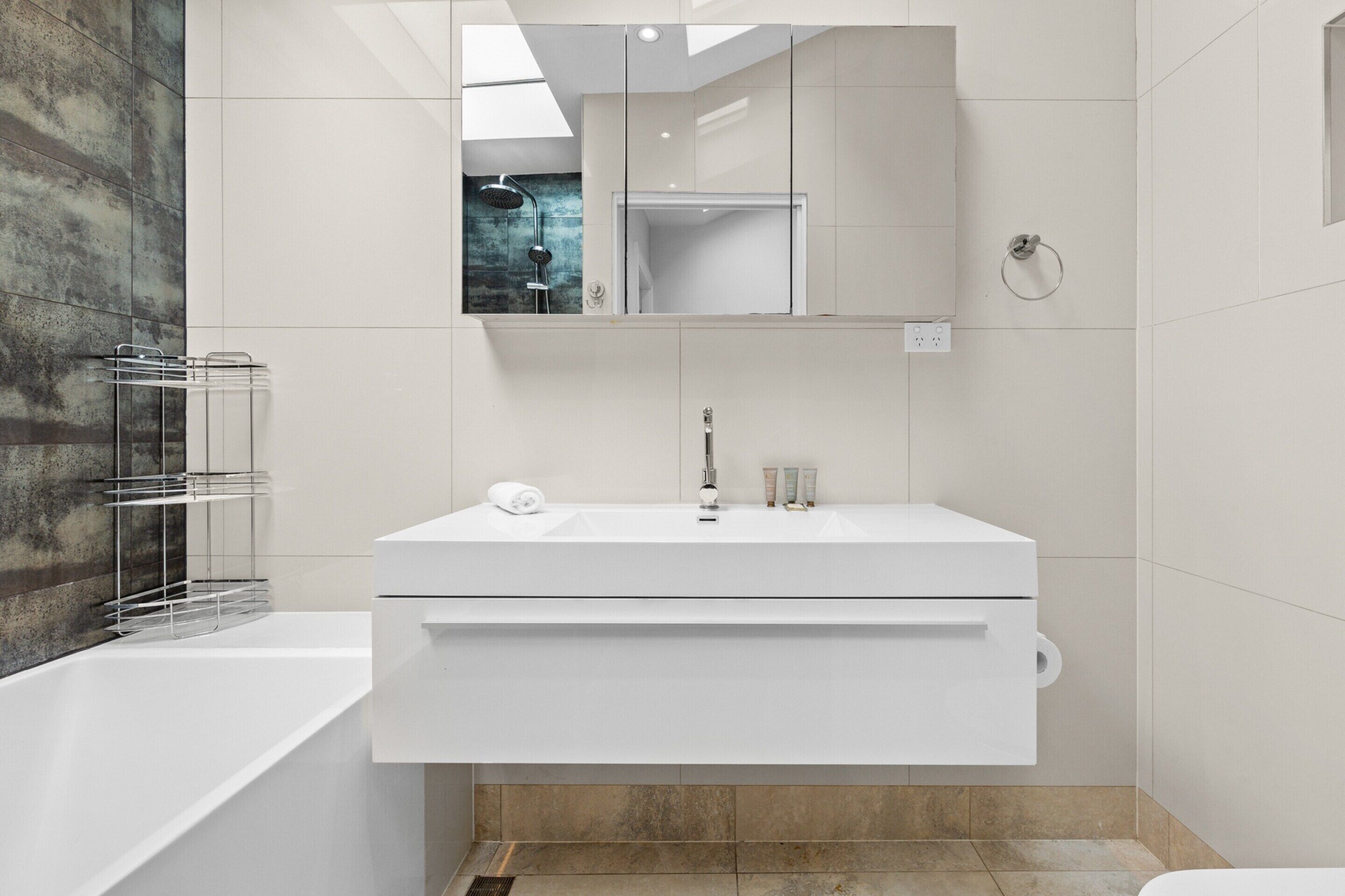 A modern bathroom with a white vanity, a glass shower enclosure, and a large mirror above the sink.