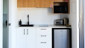 Una cocina compacta con armarios blancos, microondas, cafetera y un refrigerador pequeño.